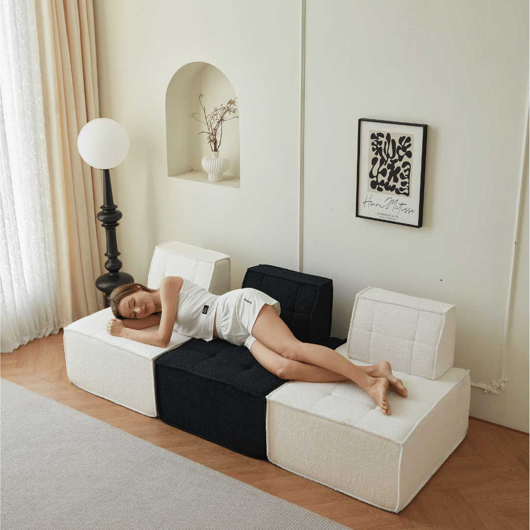 Woman peacefully napping on a modular Matoresu TofuSeat™ sofa setup in black and white sherpa, highlighting comfort and versatility in a cozy minimalist room