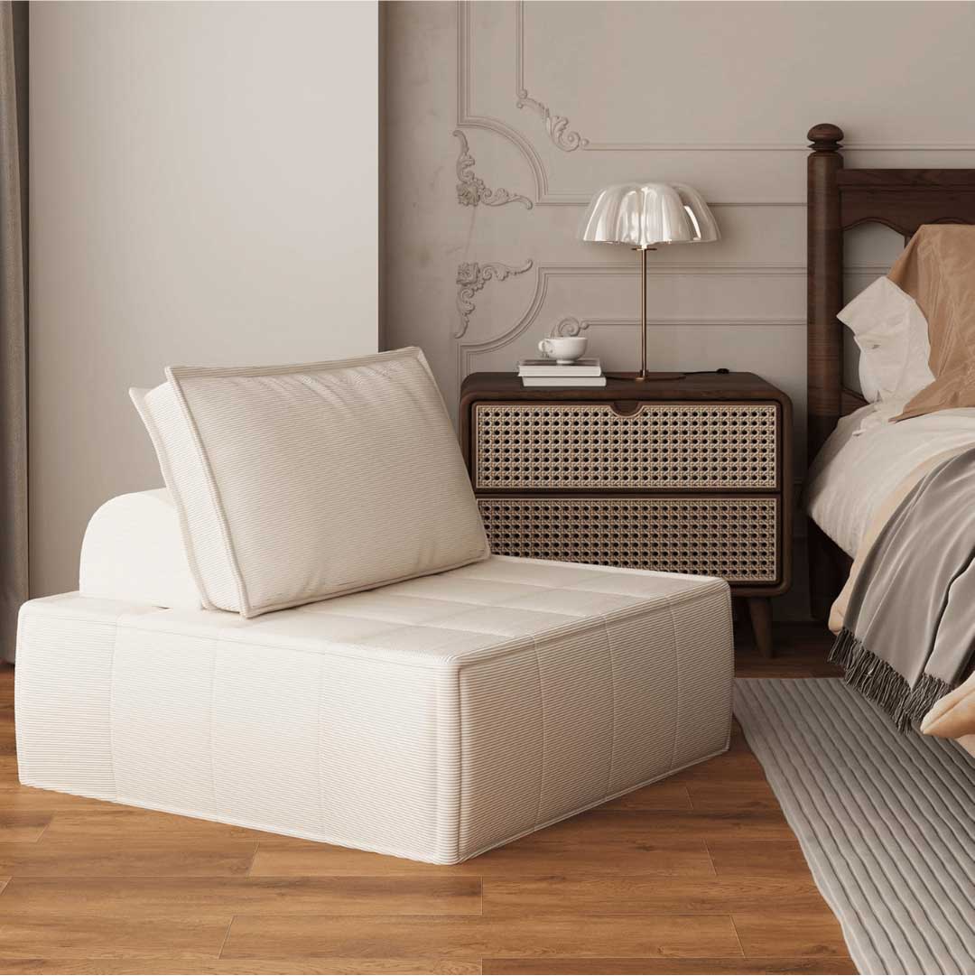 Modular armless corduroy chair in beige next to a classic wood bed and rattan nightstand