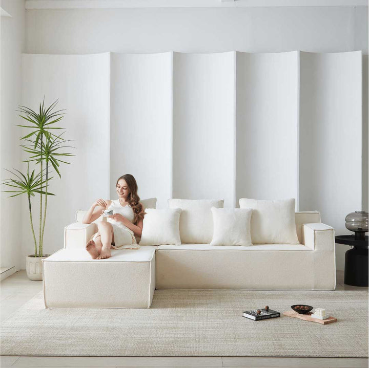 Woman relaxing on Matoresu CloudNest white memory foam sectional sofa with chaise, enjoying coffee in a minimalist living room